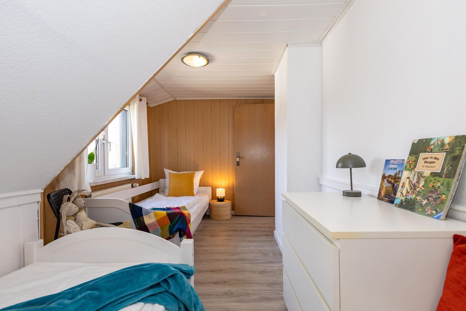 Zimmer mit zwei Betten, Schrank und Fenster unter Dachschräge.