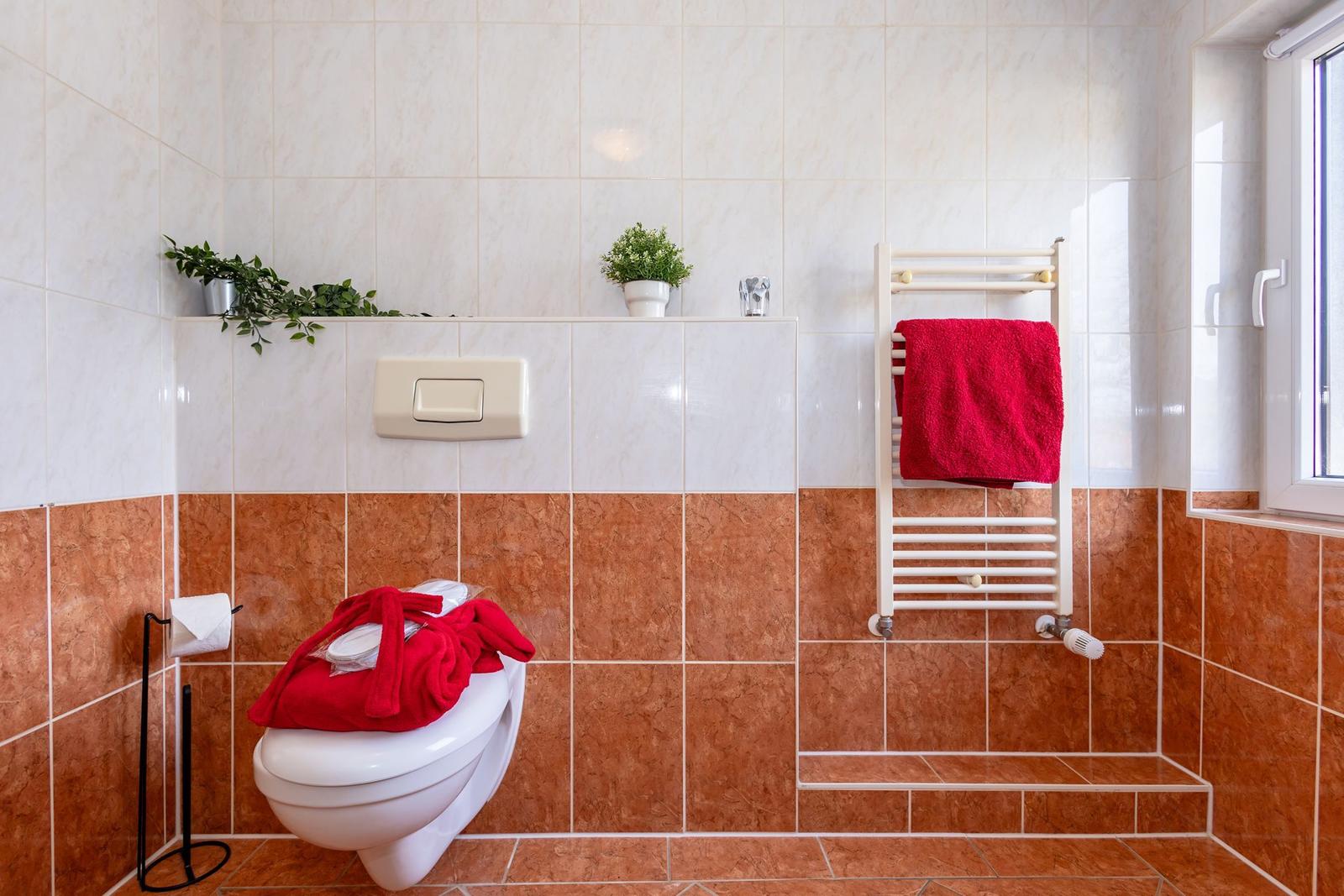 Badezimmer mit Toilette, Handtuchhalter und Fenster.
