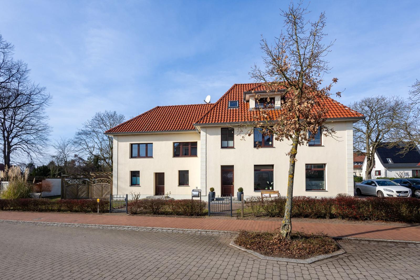 Zweistöckiges Haus mit rotem Dach und Vorgarten. Eingangstür und Fenster sind sichtbar.