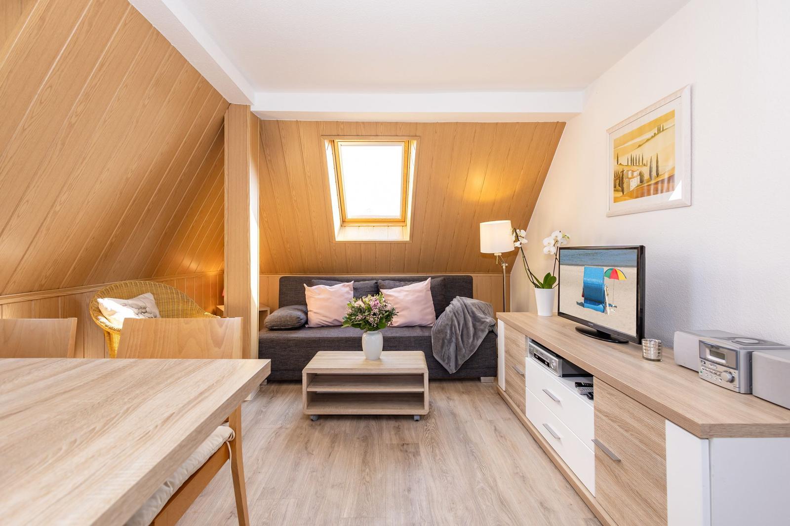Wohnbereich mit Sofa, TV und Essbereich unter Holzdecke.