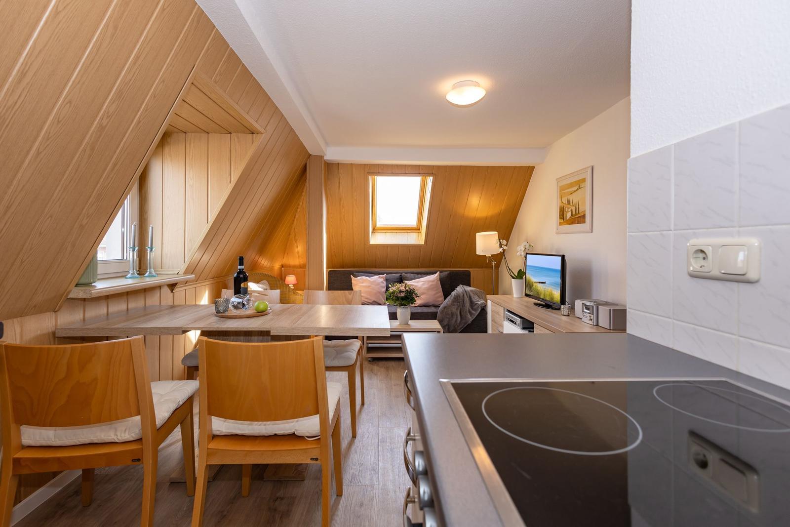 Wohnküche mit Esstisch, Sofa und TV unter Holzdecke.