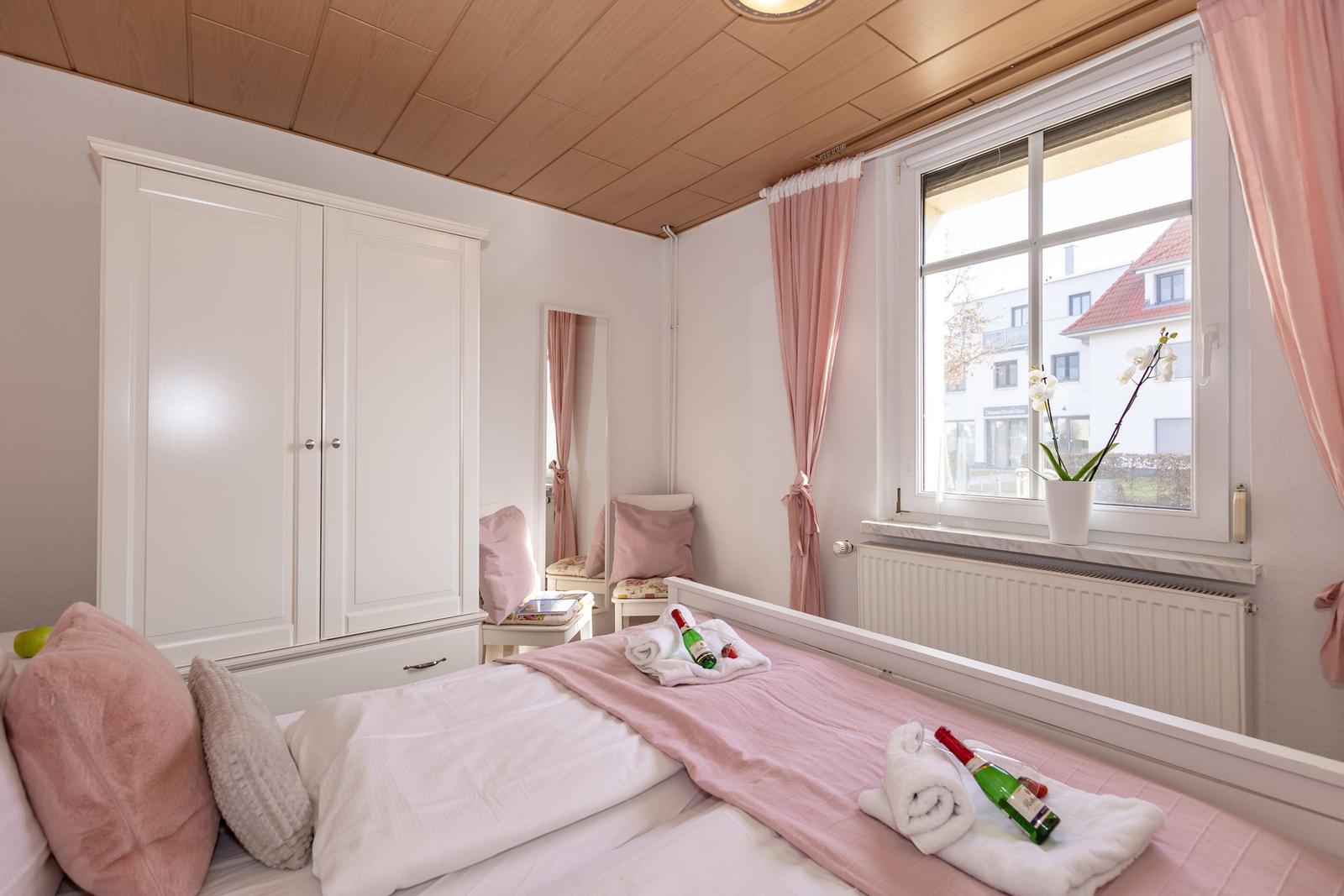 Schlafzimmer mit Bett, Kleiderschrank und Fenster mit rosa Vorhängen.