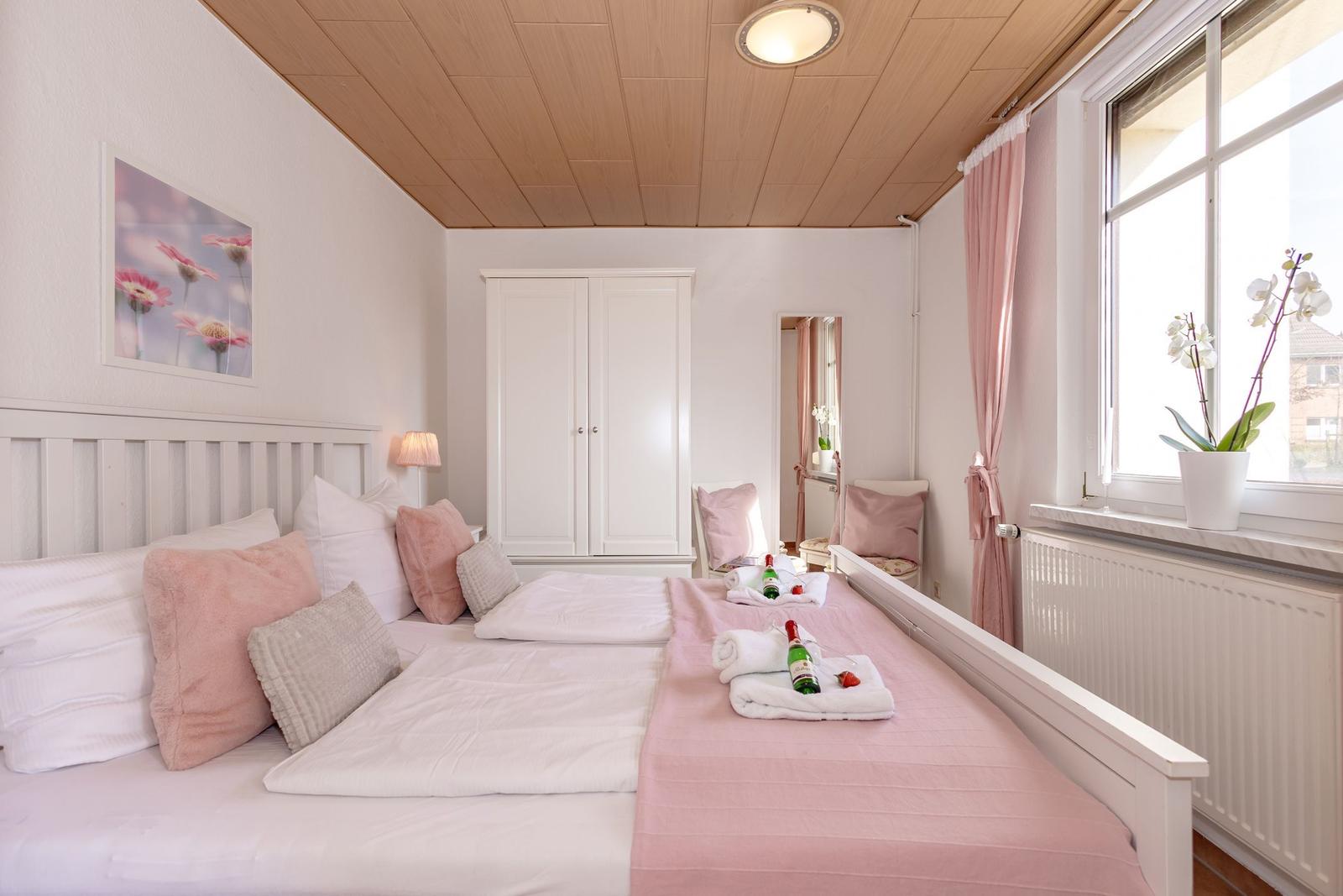 Schlafzimmer mit Doppelbett, rosa Decke, Fenster und Schrank.