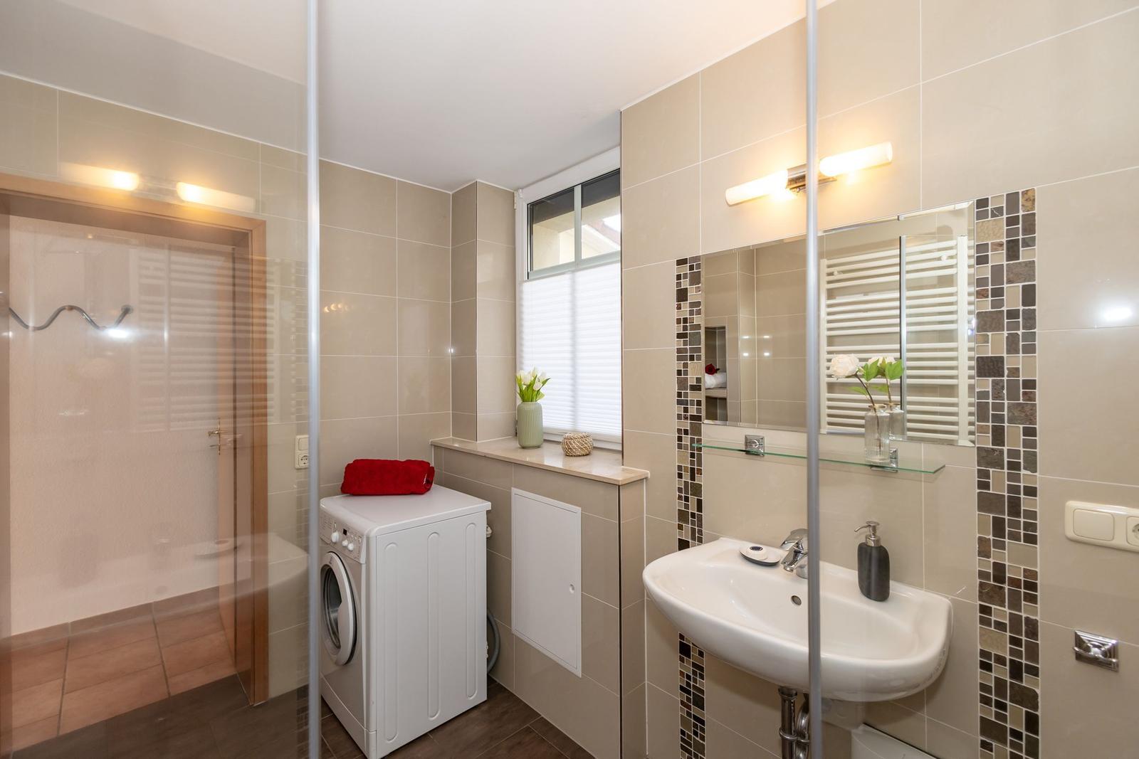 Badezimmer mit Waschmaschine, Spiegel und Dusche.