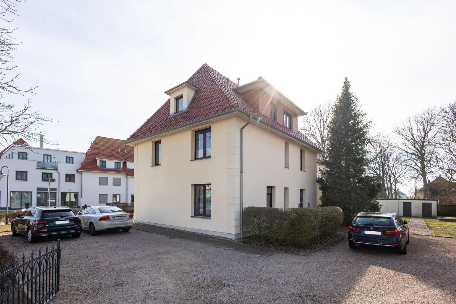 Haus mit rotem Dach und gepflastertem Hof. Drei Autos stehen auf dem Grundstück.