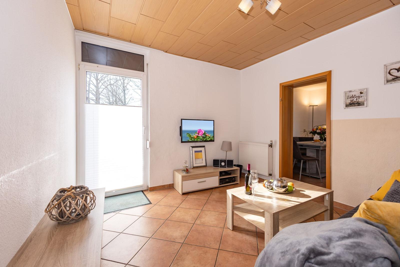 Wohnzimmer mit Fernseher, Tisch und Fenster. Blick in benachbarte Räume.