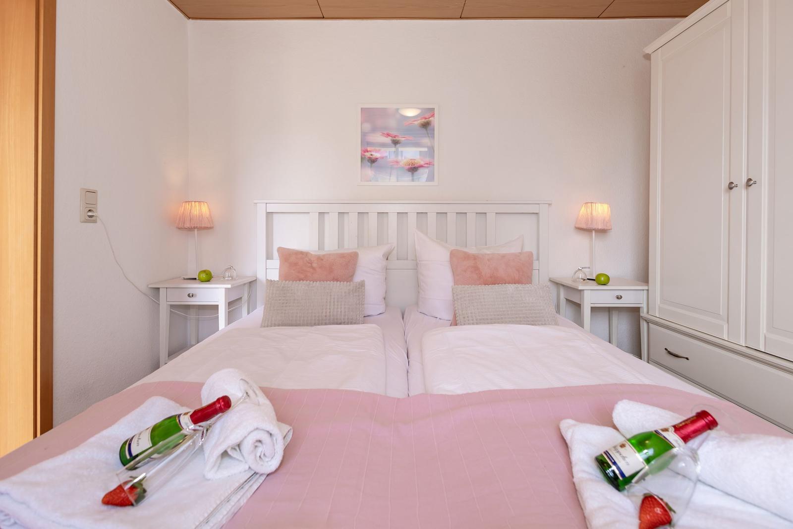 Schlafzimmer mit Doppelbett, Nachttischen und Kleiderschrank. Auf Bett liegen Flaschen und Handtücher.