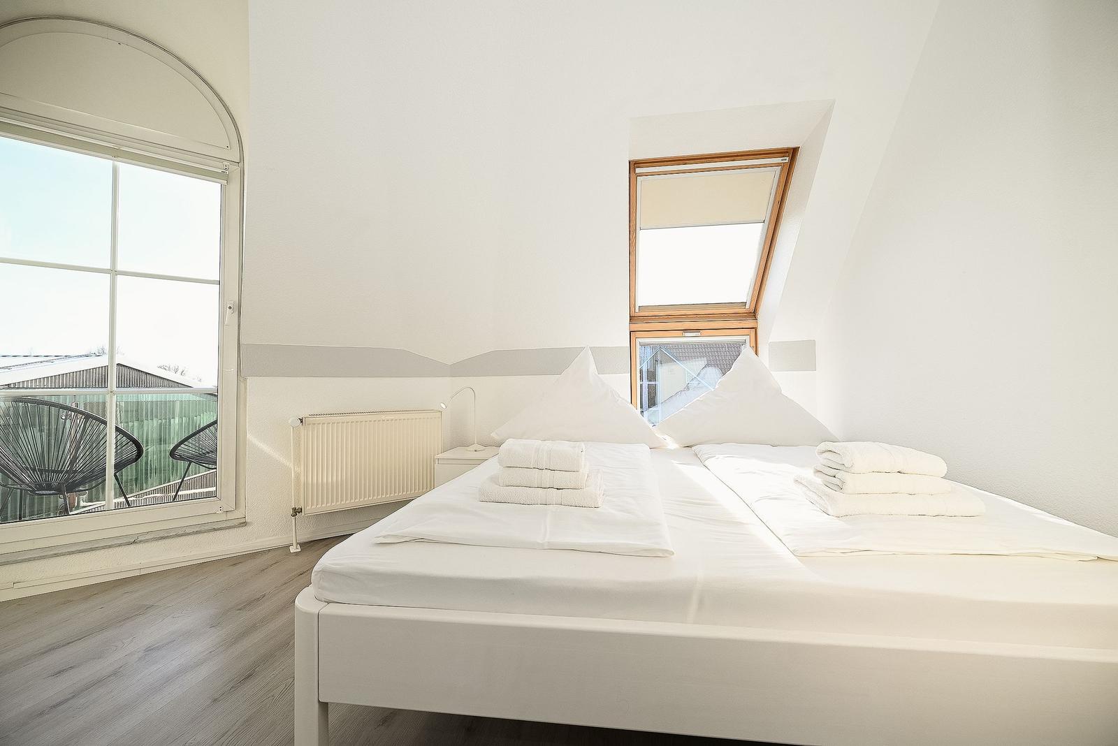 Schlafzimmer mit Dachschräge, großem Fenster und weißem Bett.