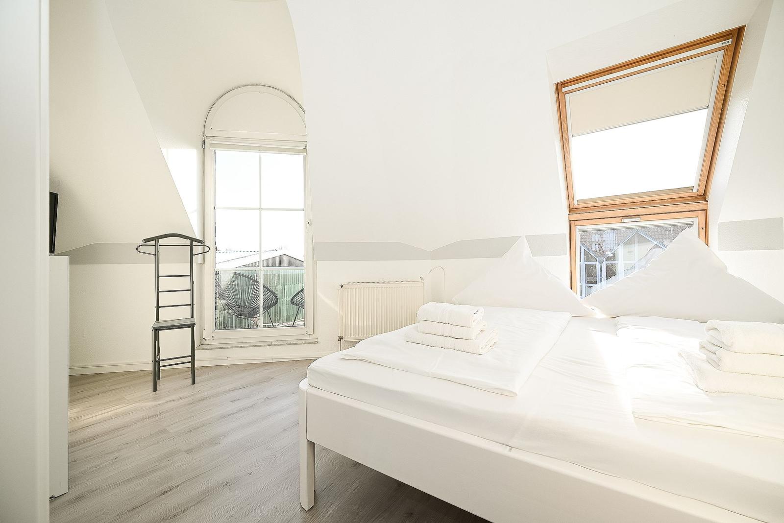 Schlafzimmer mit Doppelbett, zwei Fenstern und Holzboden.