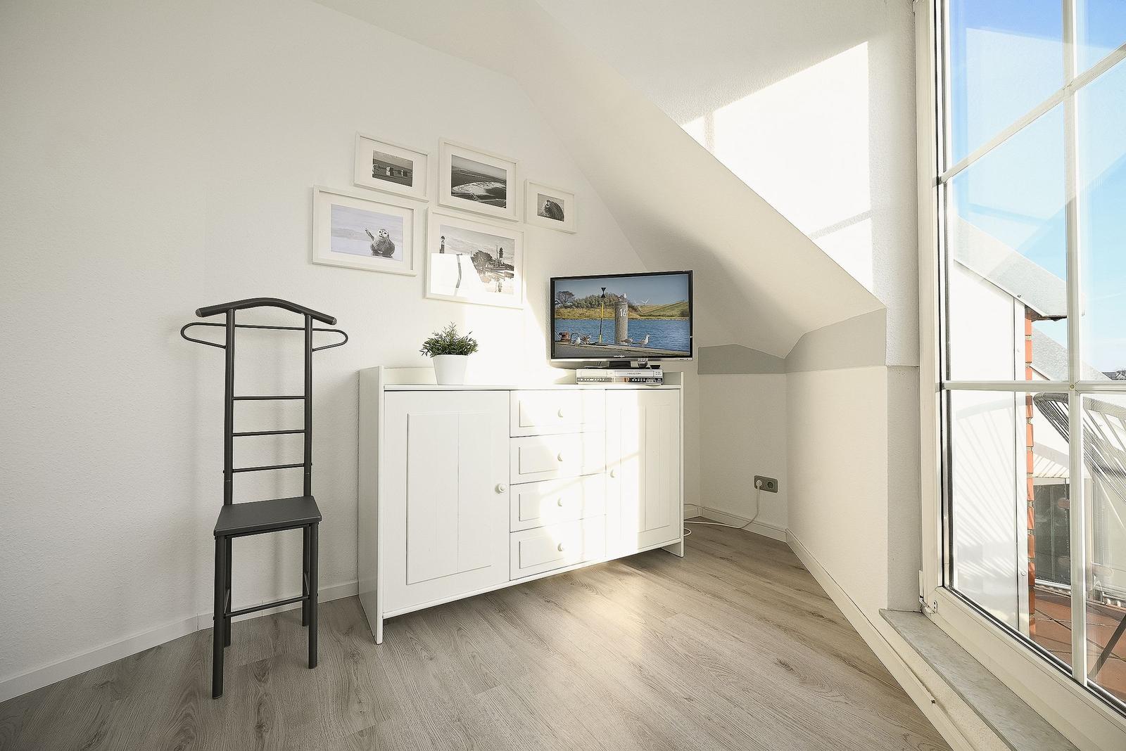 Schlafzimmer mit TV, Kleiderständer und großem Fenster.