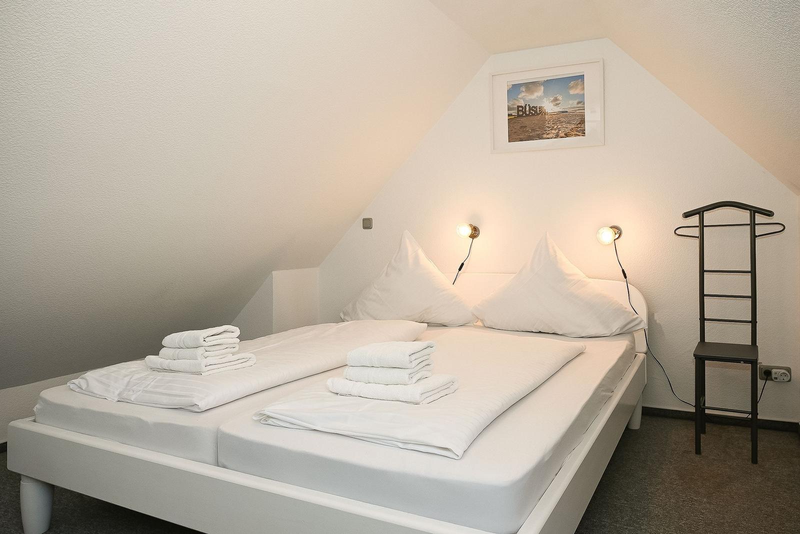 Schlafzimmer mit Doppelbett, weißen Laken und zwei Wandlampen.