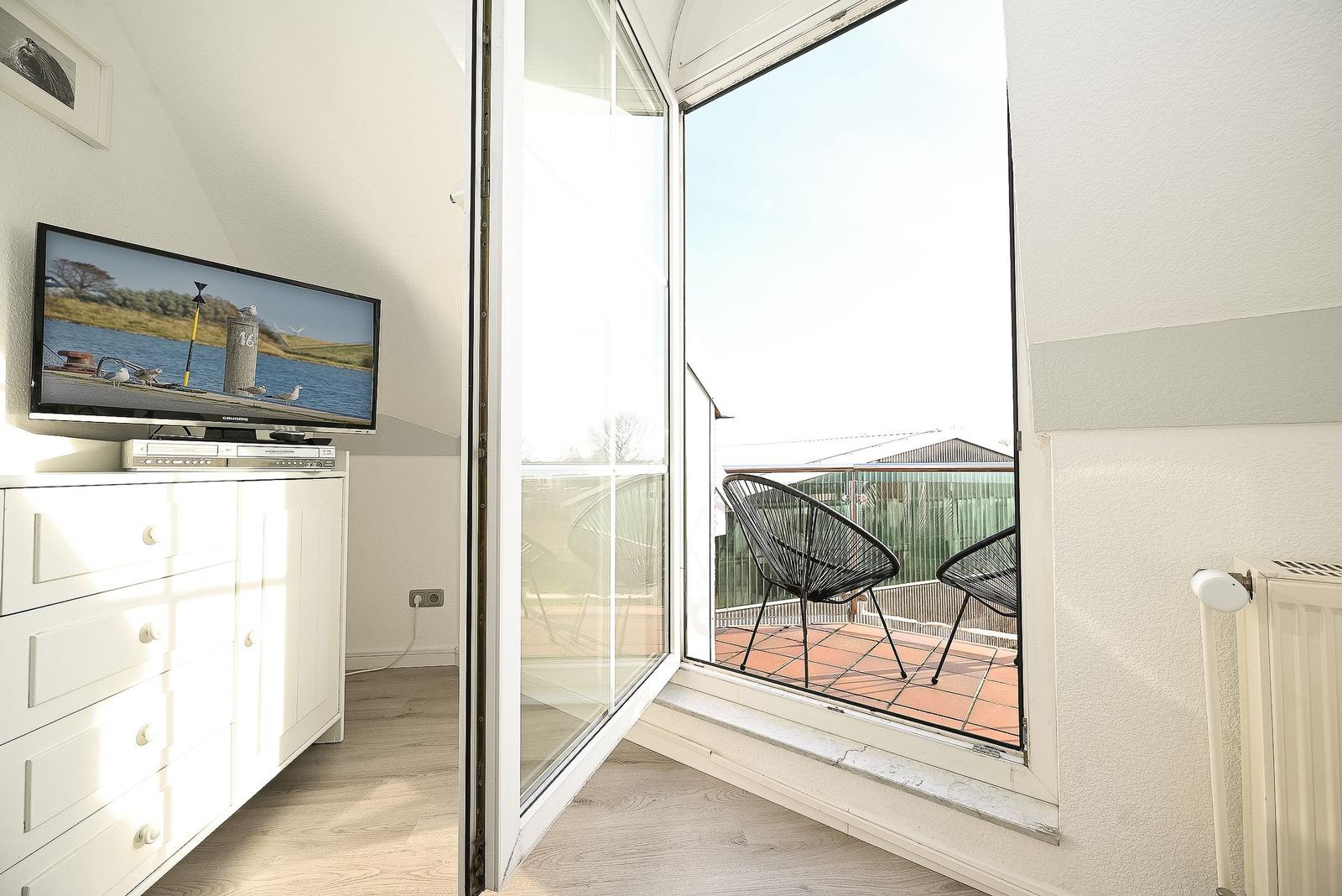 Wohnzimmer mit TV und Balkon mit zwei Stühlen.