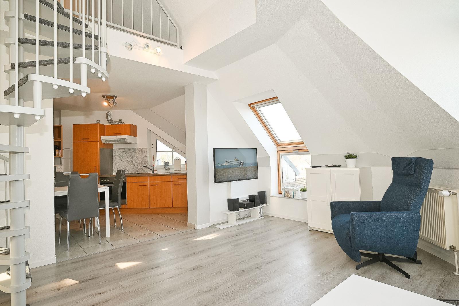 Wohnbereich mit TV, blauer Sessel und Küchenbereich im Hintergrund.