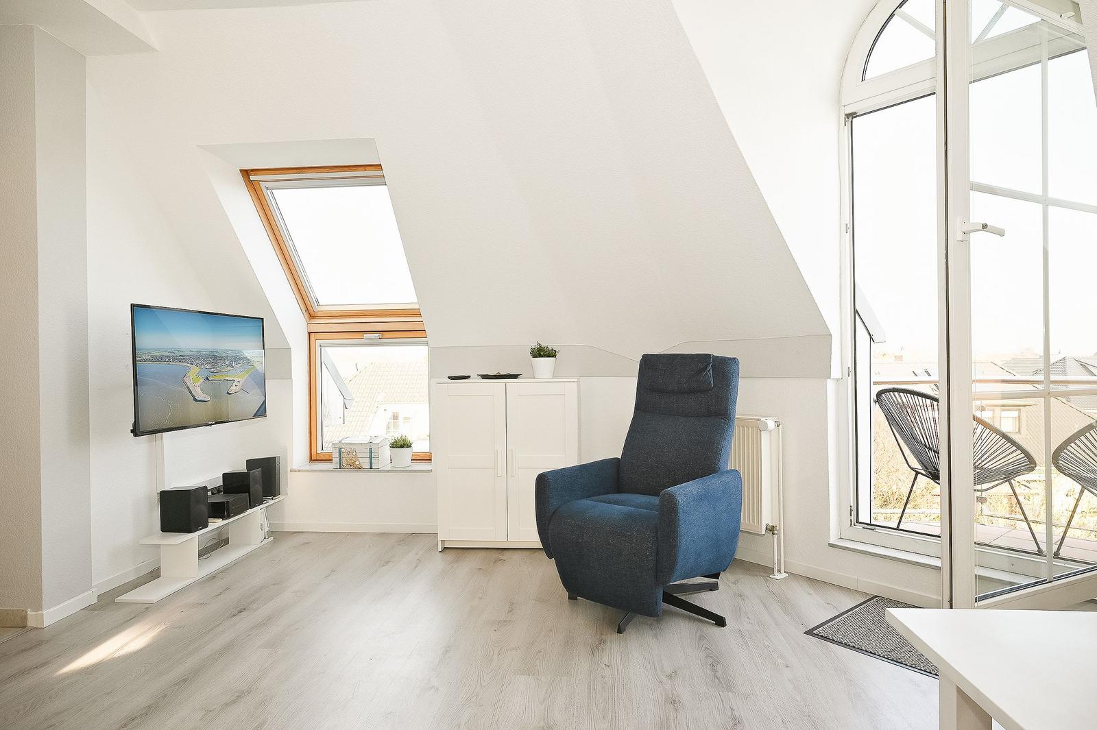 Wohnraum mit blauem Sessel, TV und Balkonansicht.