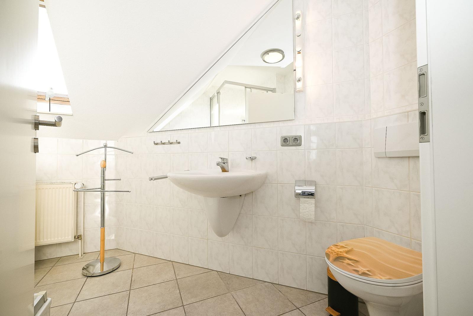 Badezimmer mit Waschbecken, Spiegel, Toilette und Dusche.