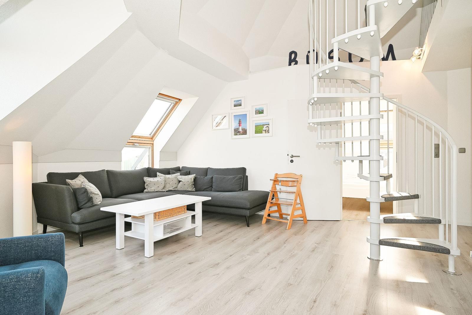 Wohnzimmer mit grauem Sofa, weißem Tisch und Wendeltreppe.
