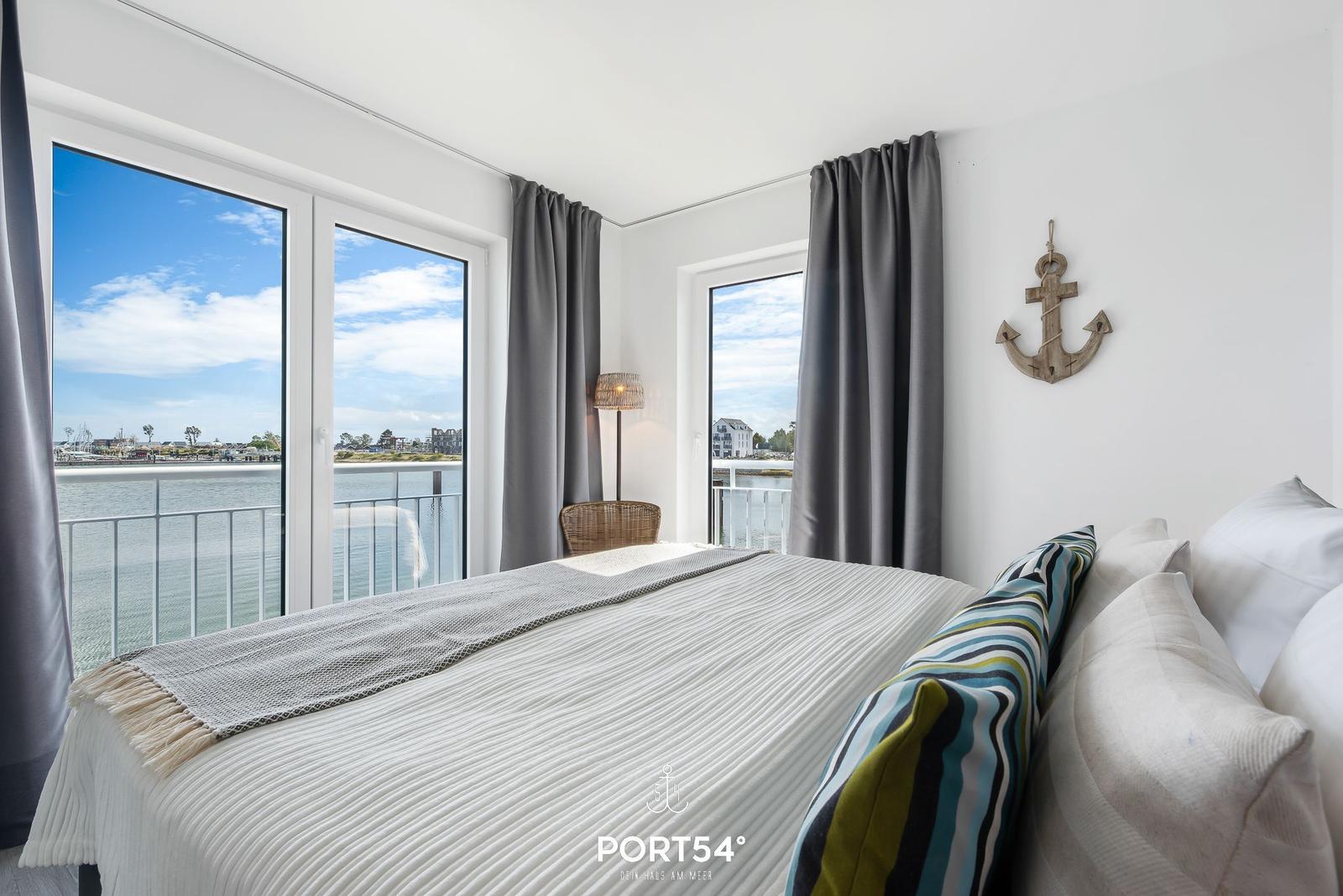 Schlafzimmer mit Blick auf Hafen und Wasser, Wanddekoration mit Ankermotiv.