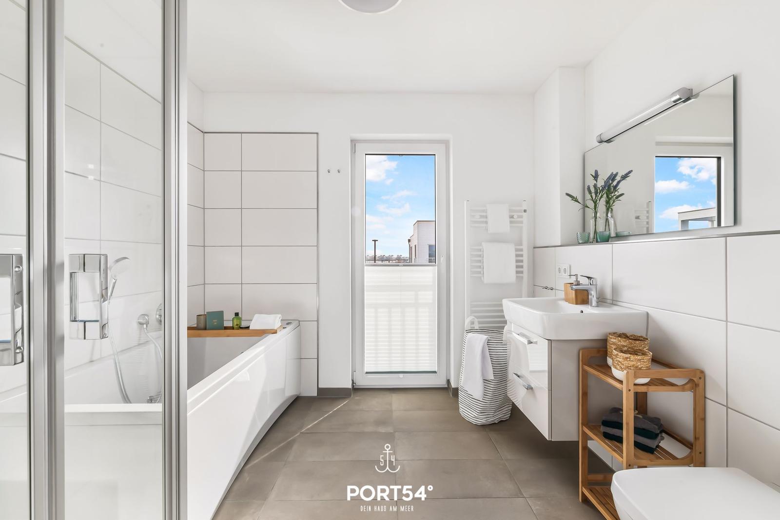 Badezimmer mit Badewanne, Dusche und Fenster zum Balkon.
