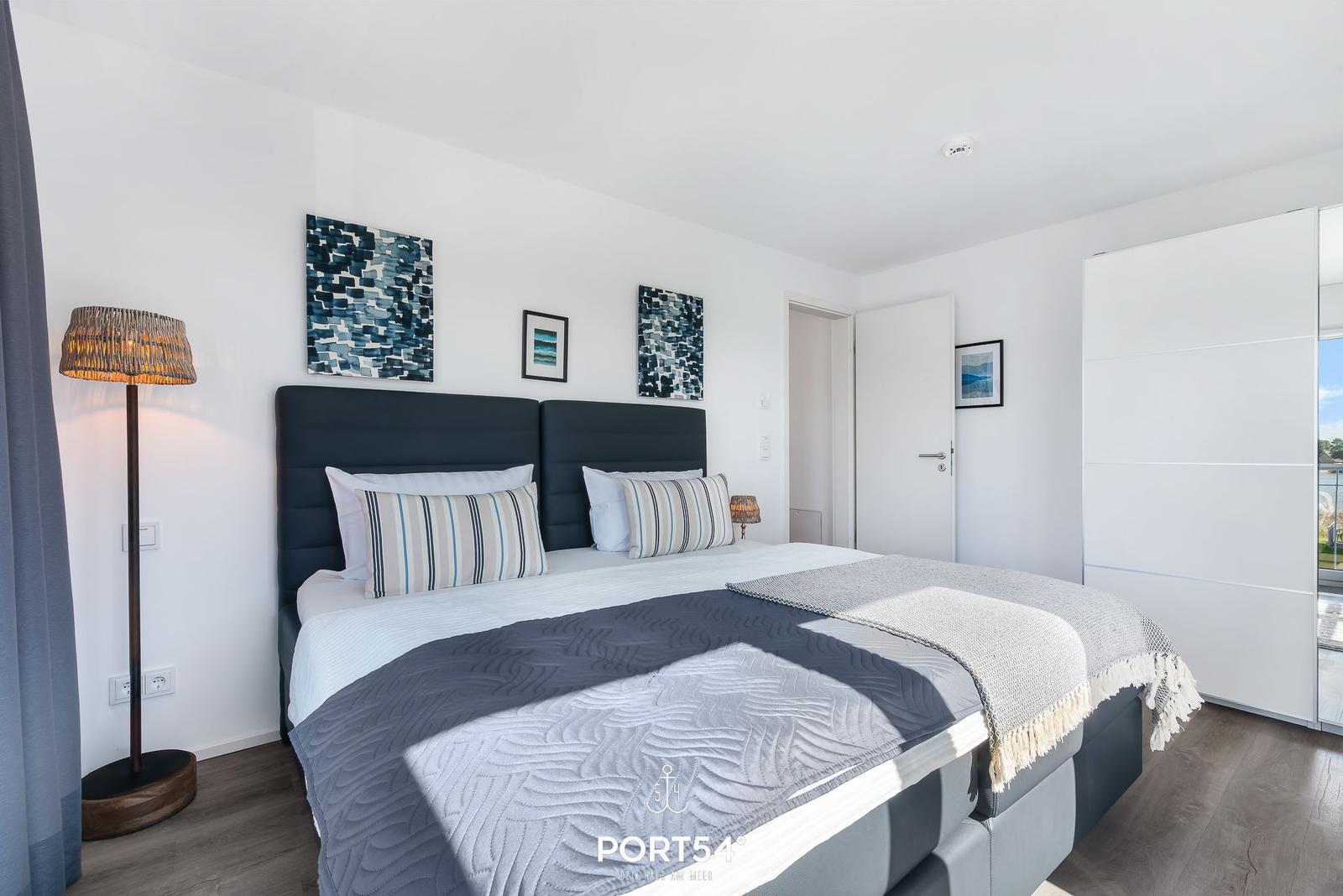 Schlafzimmer mit Doppelbett, Wandbildern und Kleiderschrank.