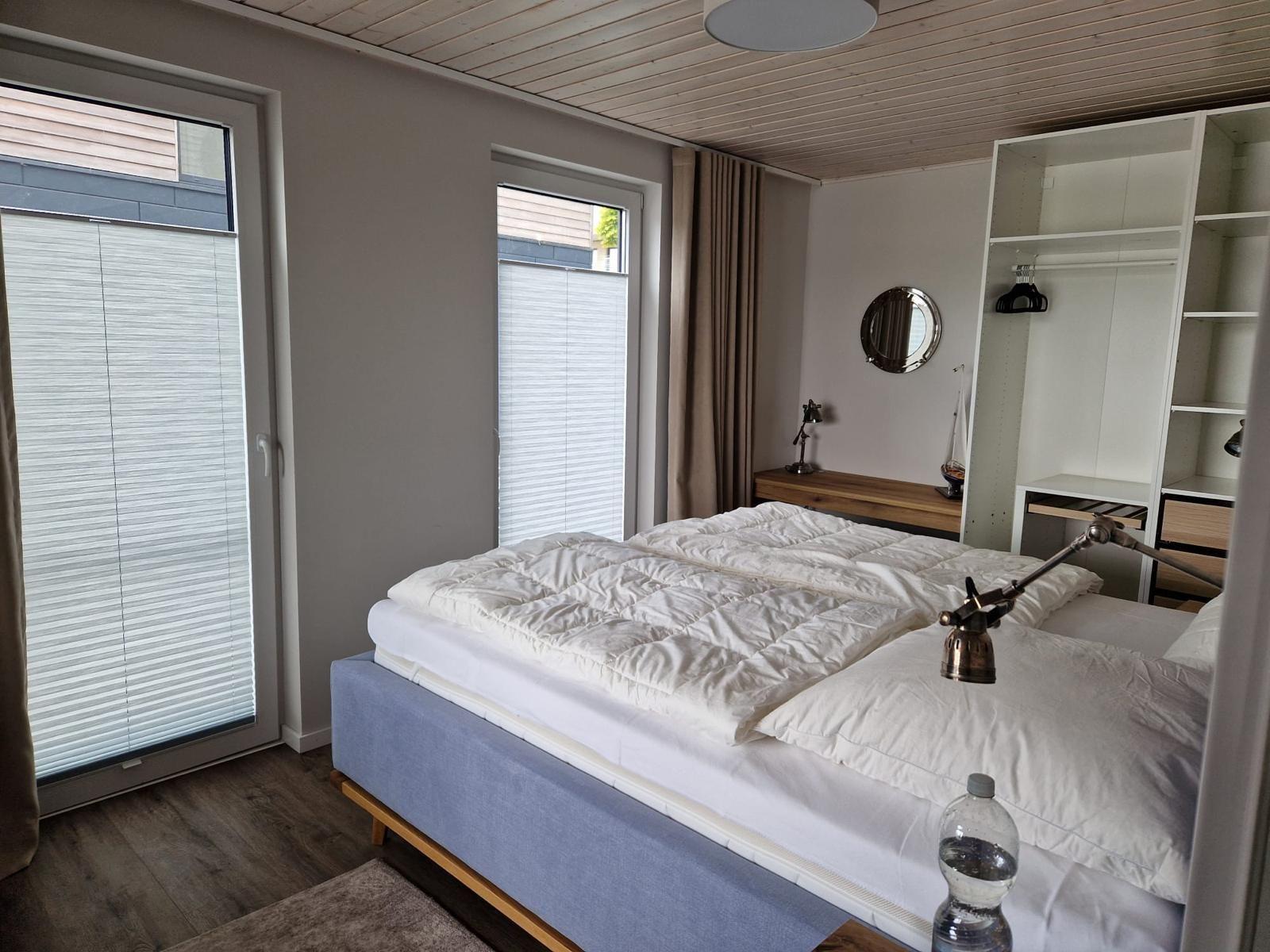 Schlafzimmer mit Bett, Kleiderschrank und Fenstern.