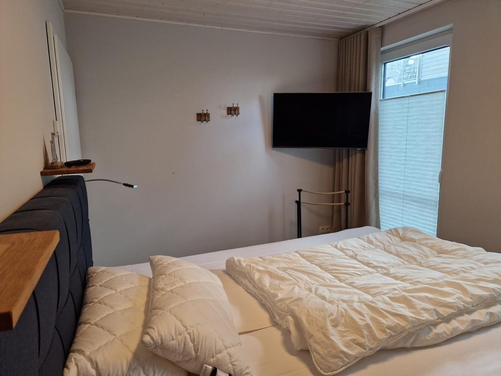 Schlafzimmer mit Bett, Fernseher und Fenster.