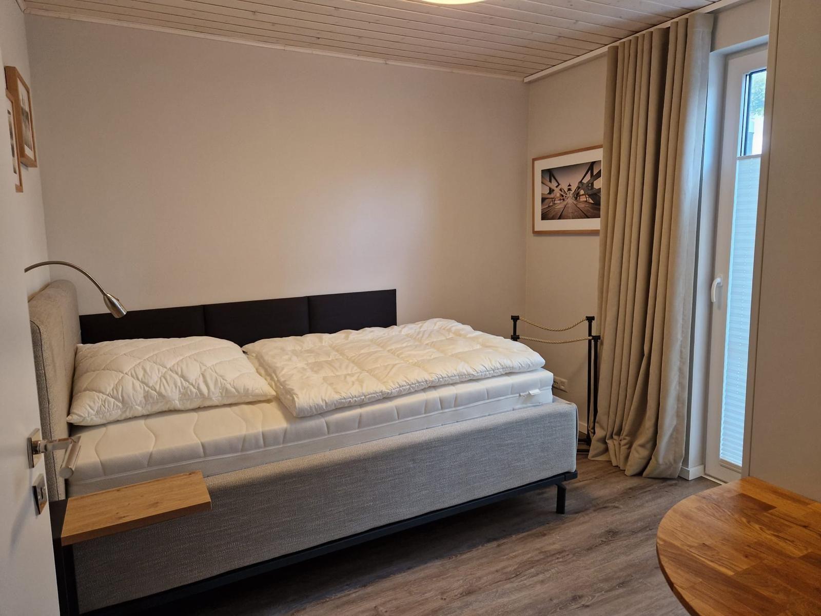 Schlafzimmer mit Bett, Nachttisch und Fenster mit Vorhängen.