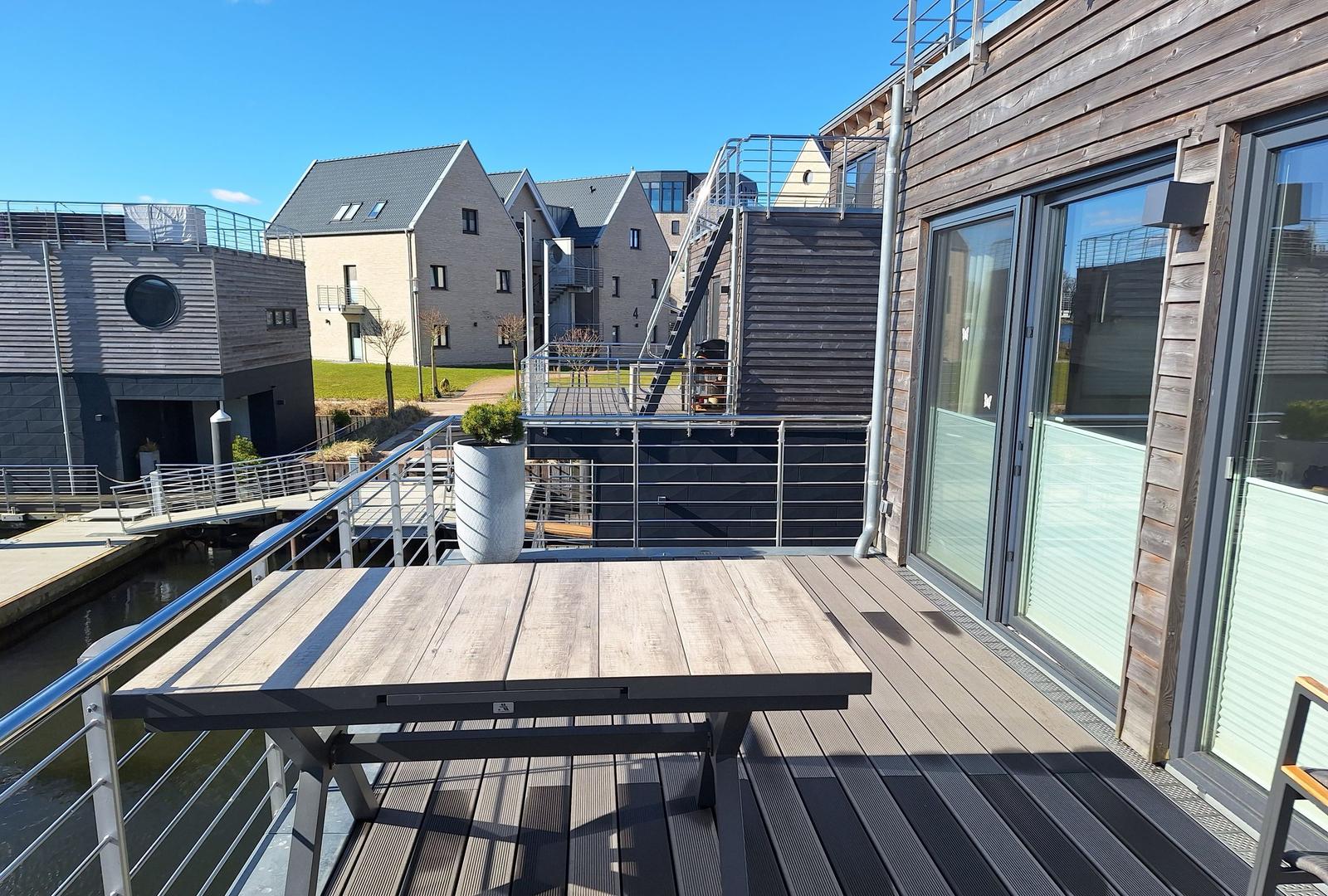 Terrasse mit Tisch und Blick auf Kanal und moderne Häuser.