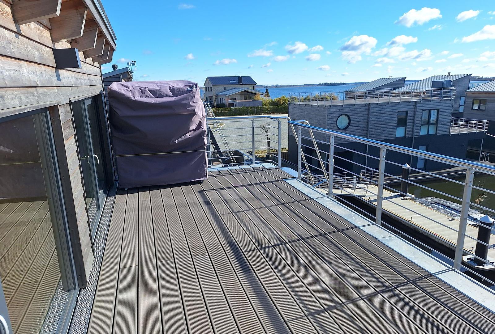 Terrasse mit Holzdecke und Blick auf Wasser und moderne Häuser.