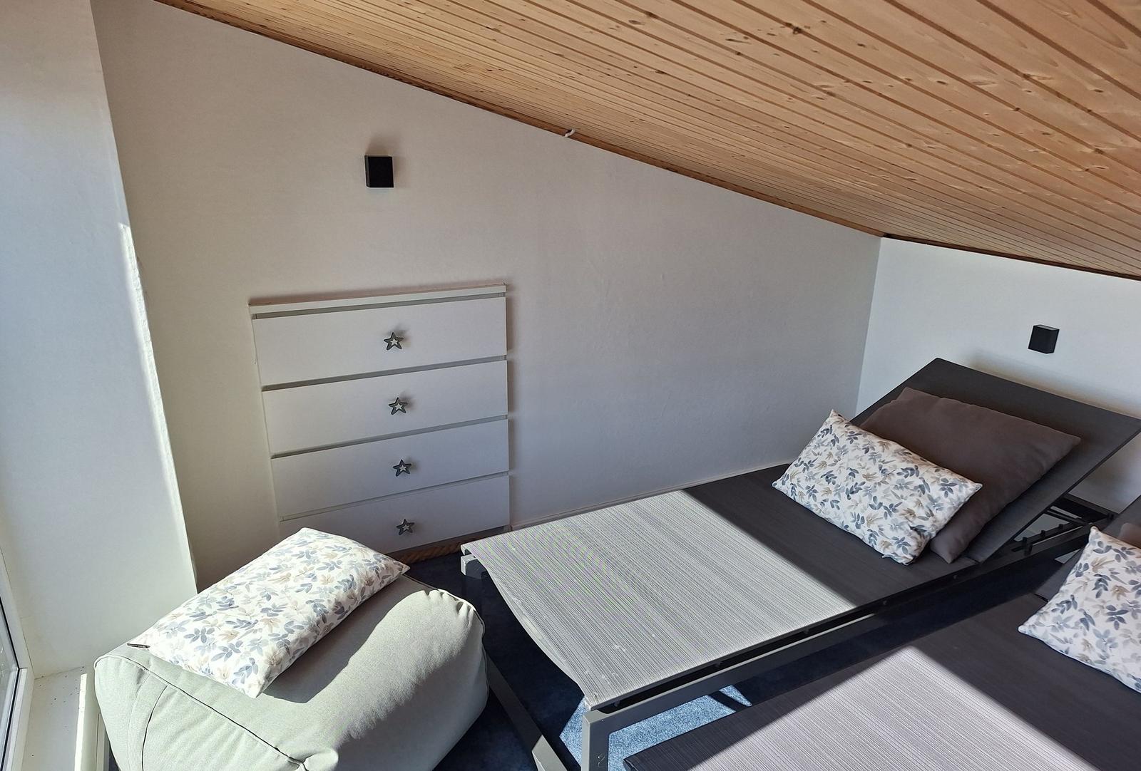 Schlafzimmer mit Bett, Kleiderschrank und Sitzkissen unter Holzdecke.