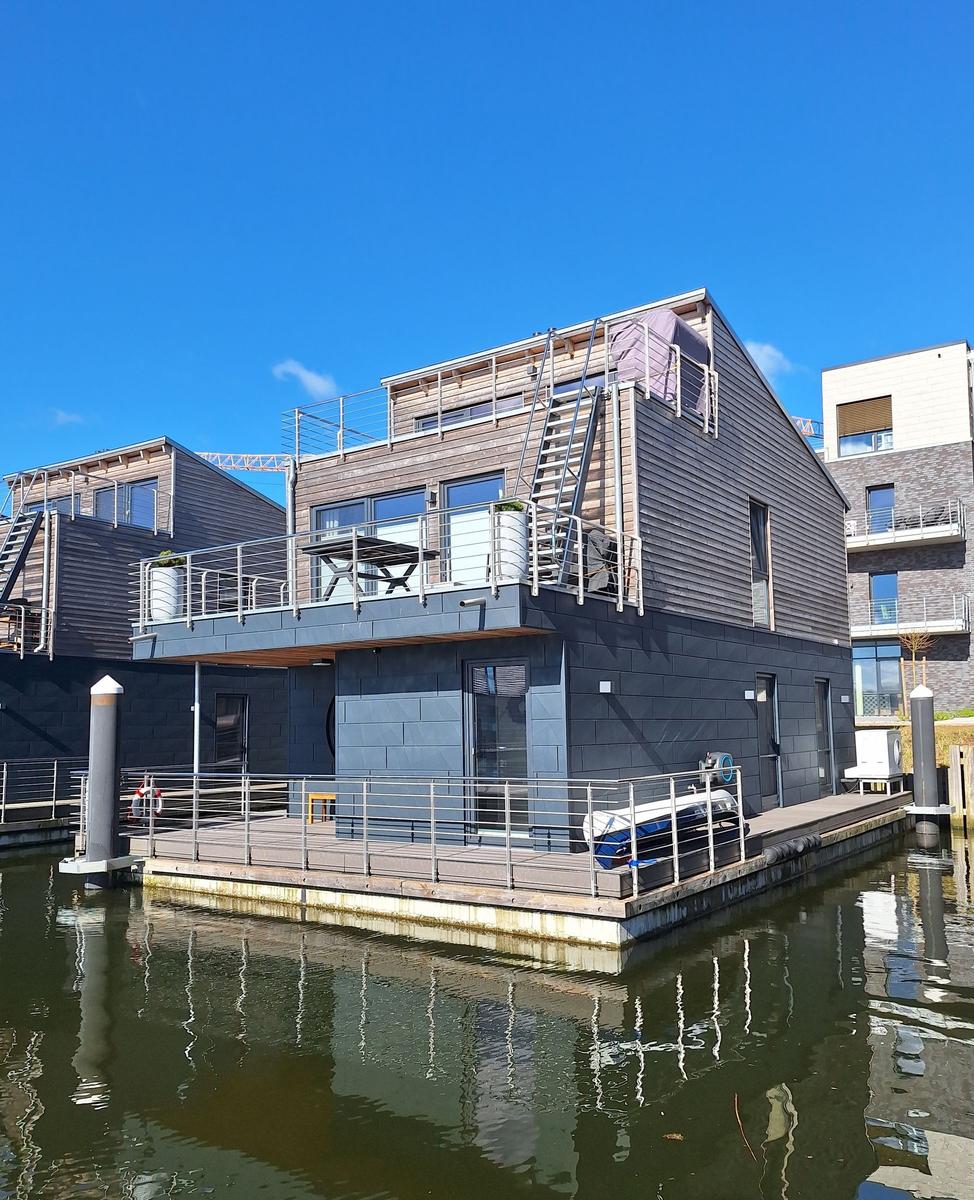 Modernes Wasserhaus mit Balkon und Bootsanlegestelle am Kanal.
