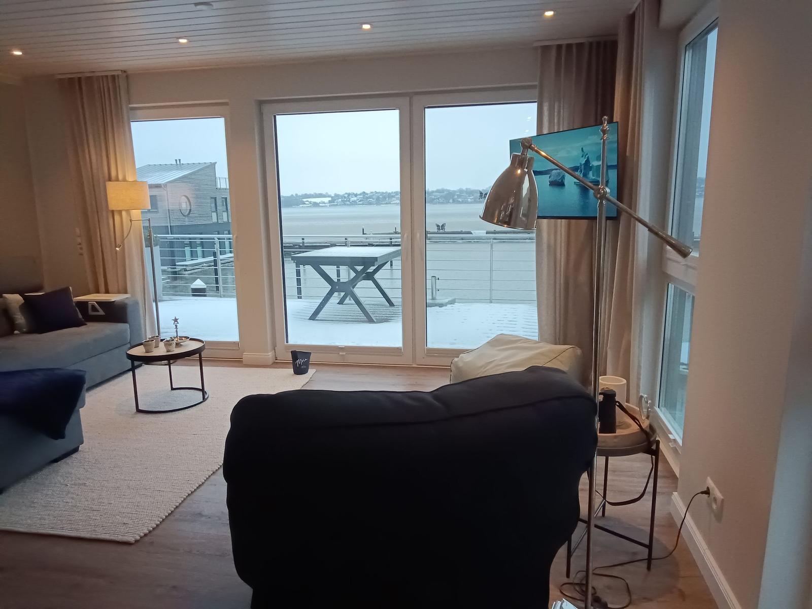 Wohnzimmer mit Blick auf den Hafen und Terrasse mit Tisch.