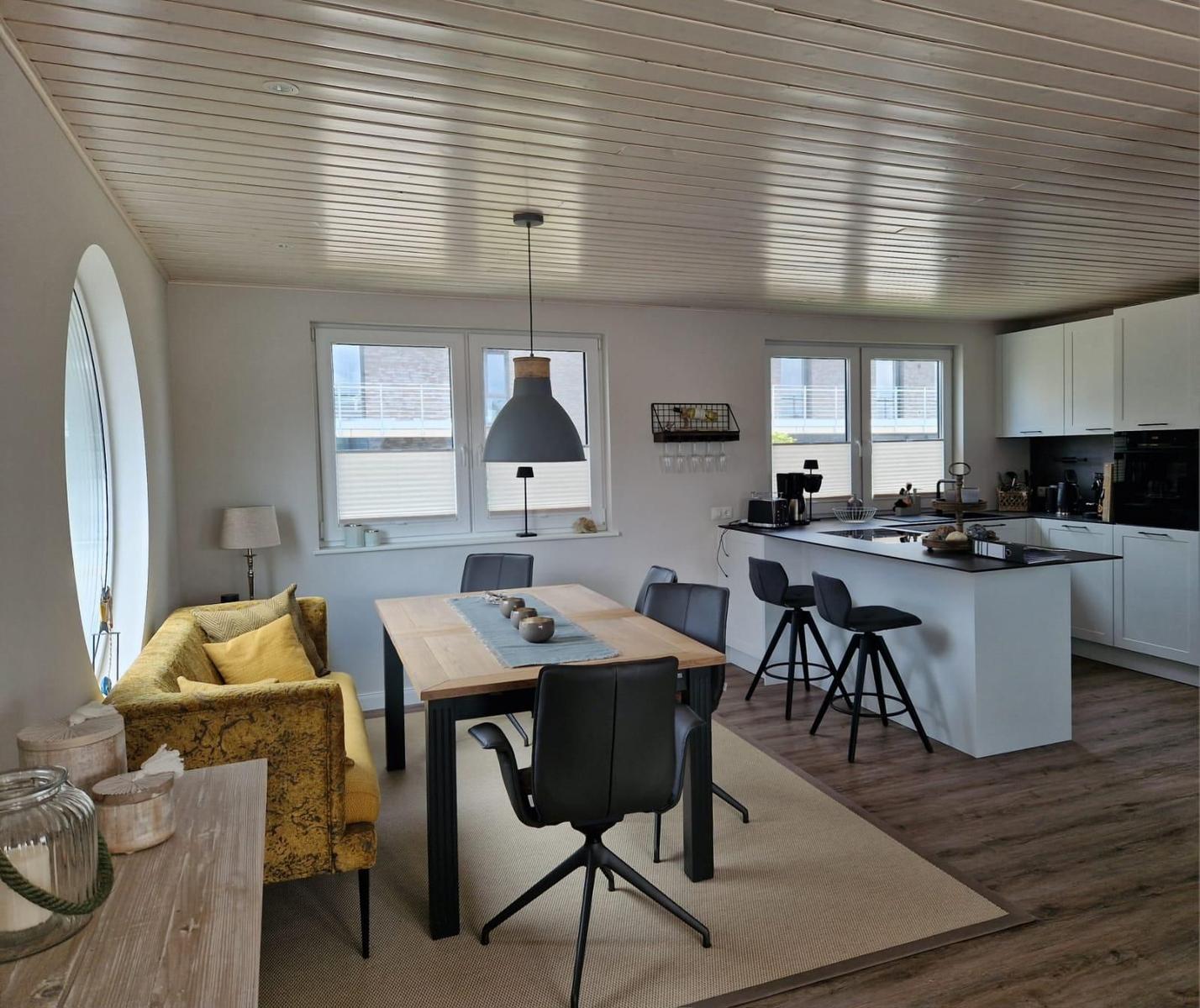 Esszimmer mit Kücheninsel und gelbem Sofa. Holzfußboden und heller Raum.
