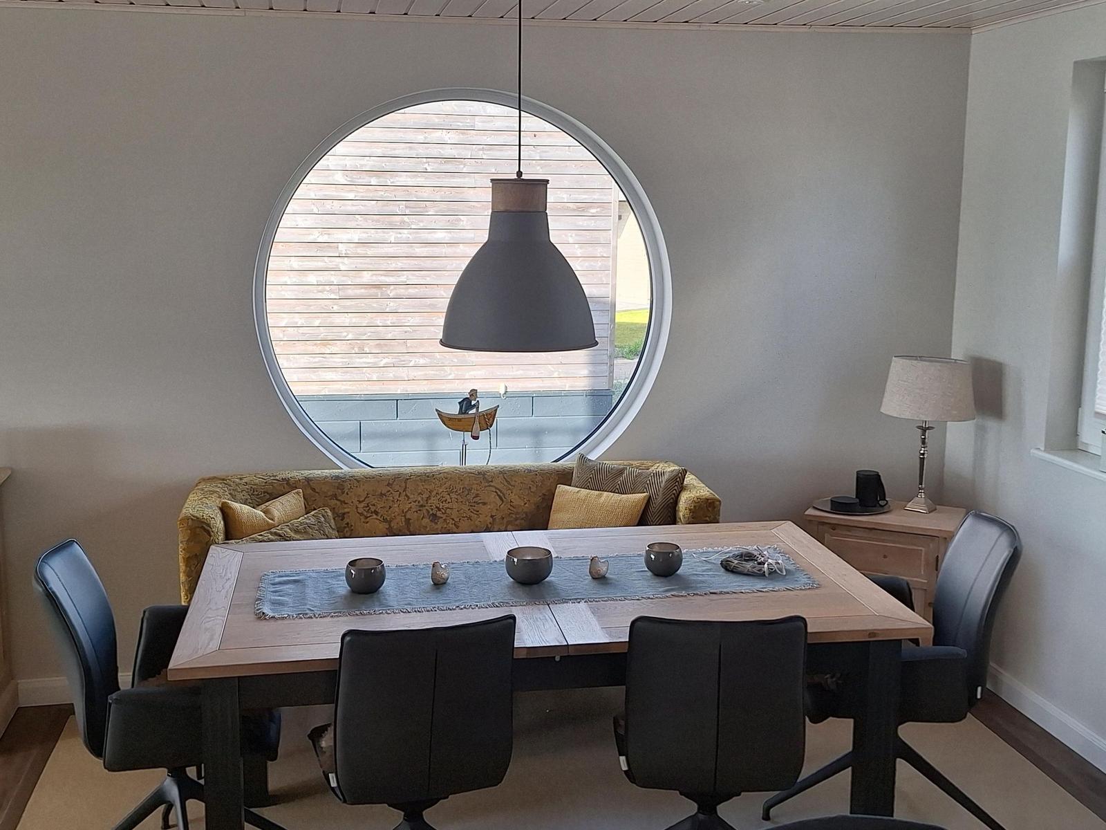 Esszimmer mit runden Fenster, Holztisch und schwarzen Stühlen.