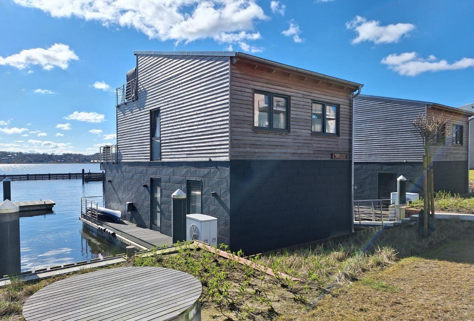 Modernes Haus am Wasser mit Holz- und Metallfassade, Bootssteg und Terrasse.