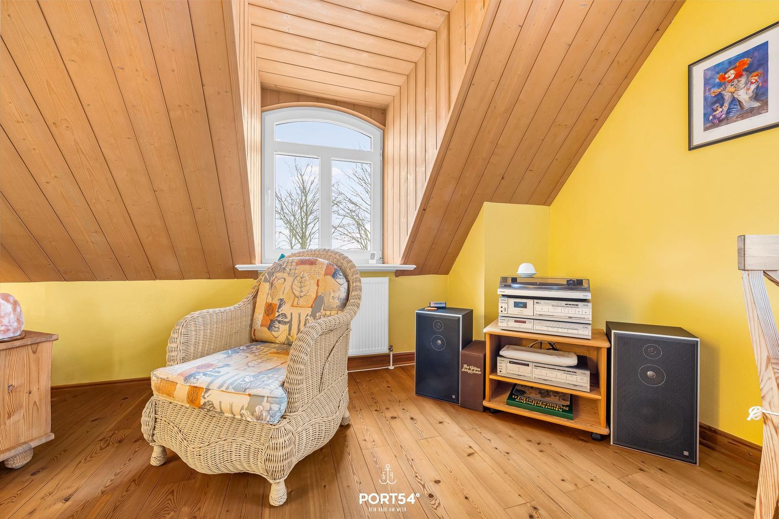 Dachgeschosszimmer mit Wickerstuhl, Vinyl-Spieler und Holzdecke.