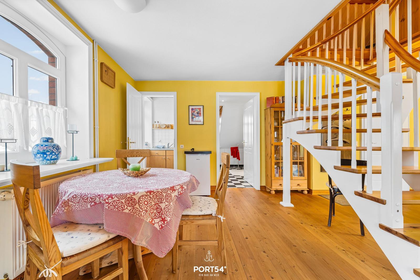 Esszimmer mit Holztisch, gelben Wänden und Holzboden. Treppe führt zur oberen Etage.