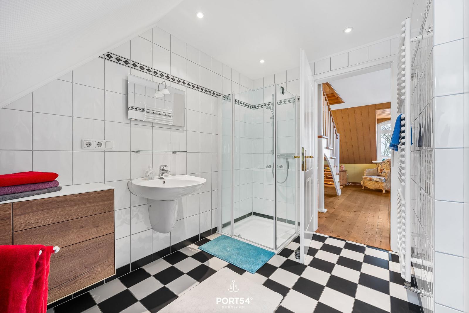 Badezimmer mit Dusche, Waschbecken und schwarz-weißem Boden