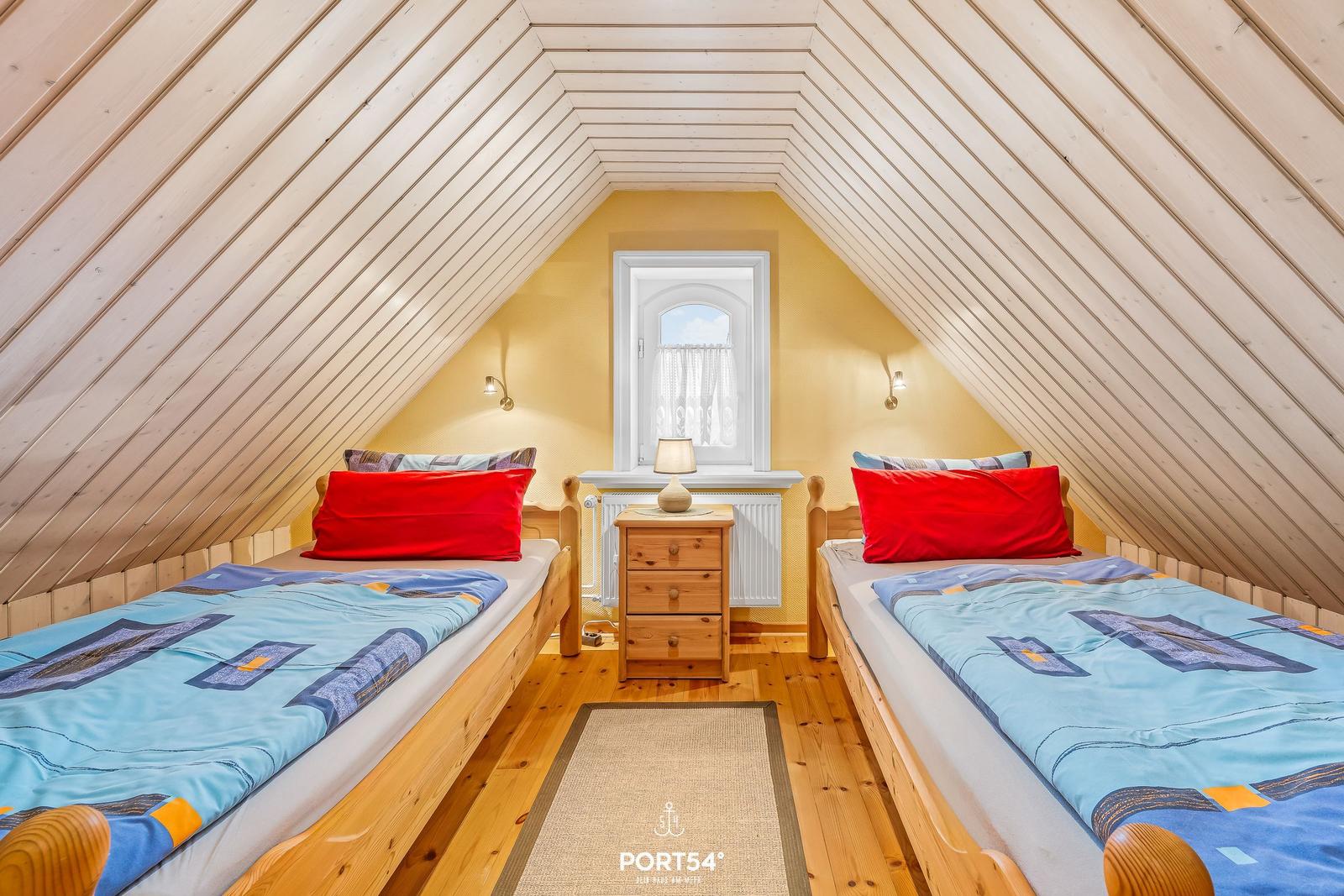 Zwei Betten mit blauen Bettwäschen unter schrägen Holzwänden.