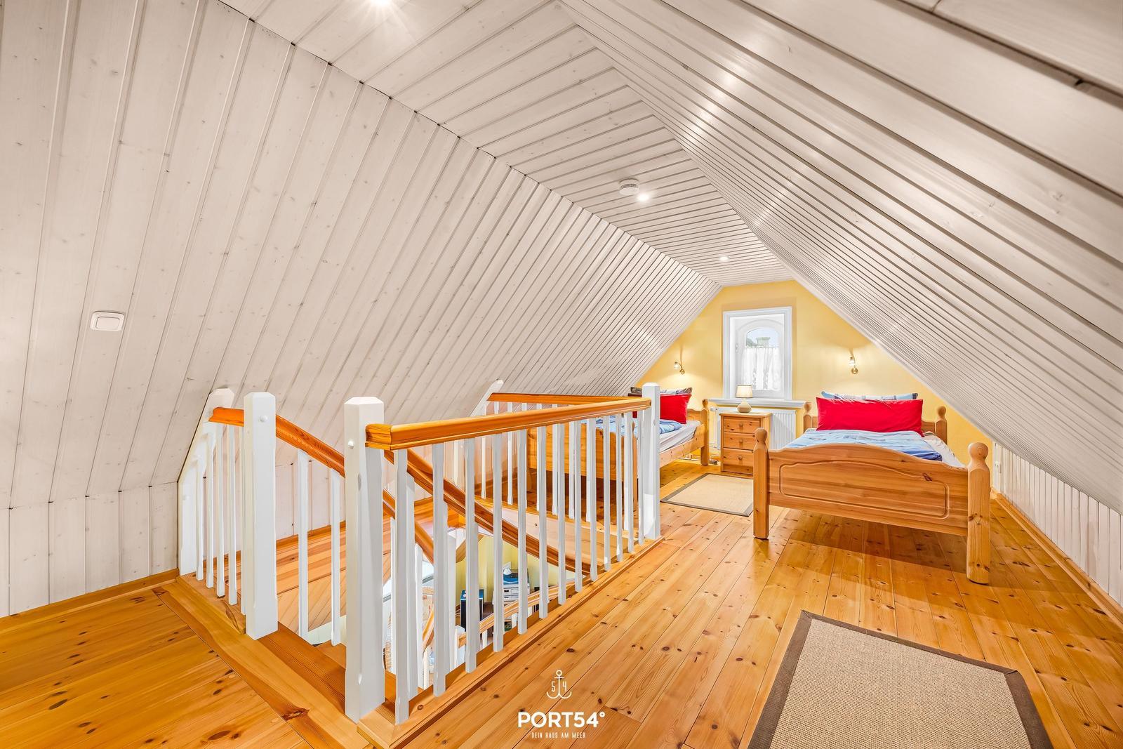 Dachgeschosszimmer mit Holzboden, zwei Betten und Holzgeländer.