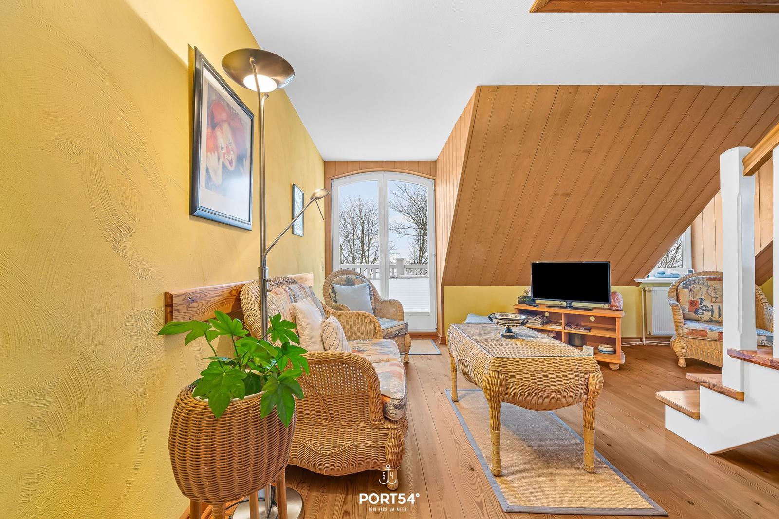 Wohnzimmer mit Rattanmöbeln, Fernseher und Balkontür.