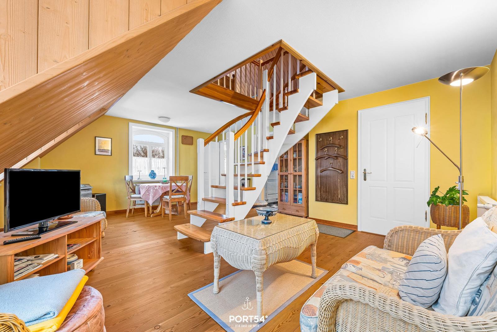 Wohnbereich mit Holzdecke, Treppe und Essbereich. Möbel aus Rattan und Holz.