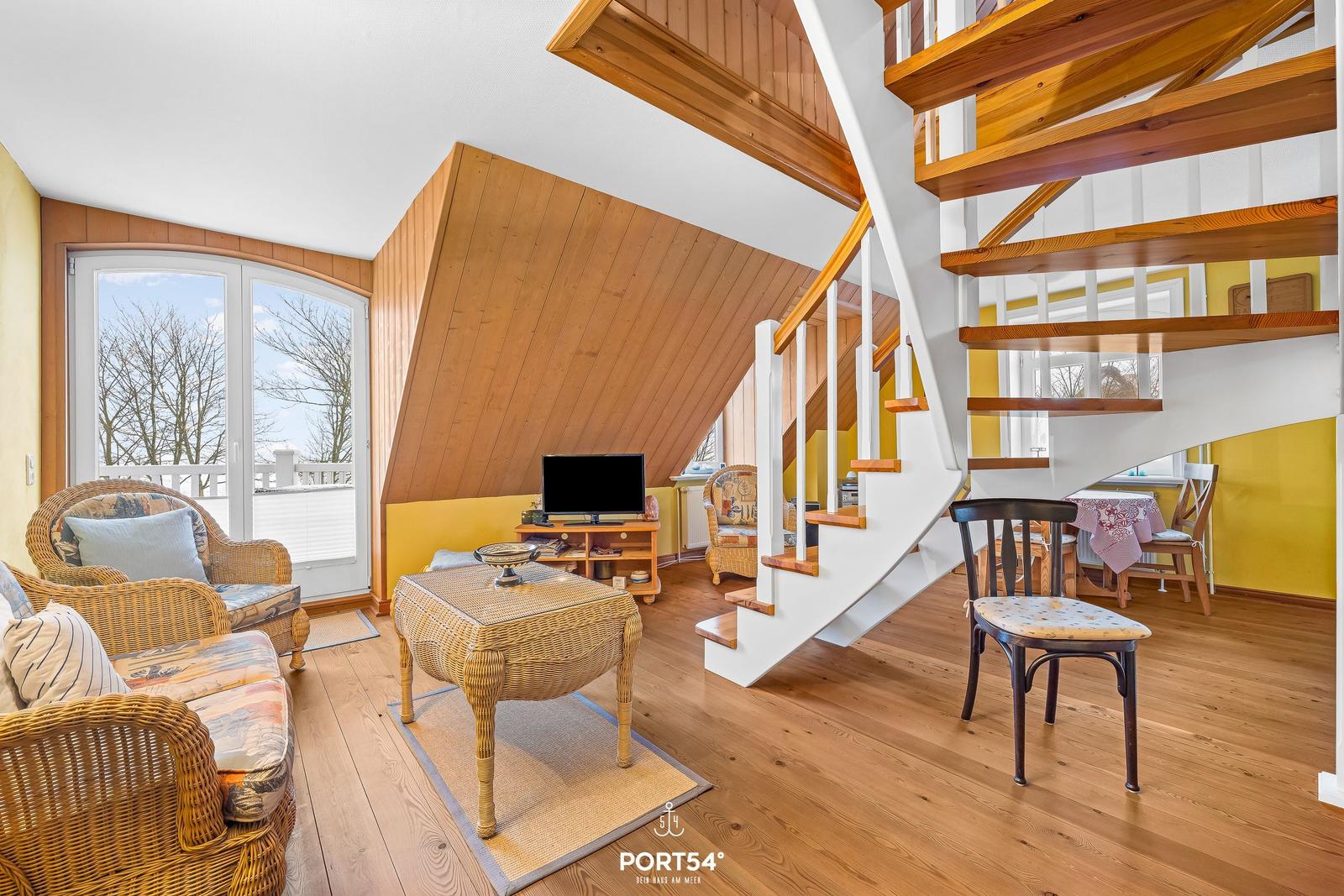 Wohnbereich mit Treppe, Sitzmöbeln und TV. Holzdecke und Boden.
