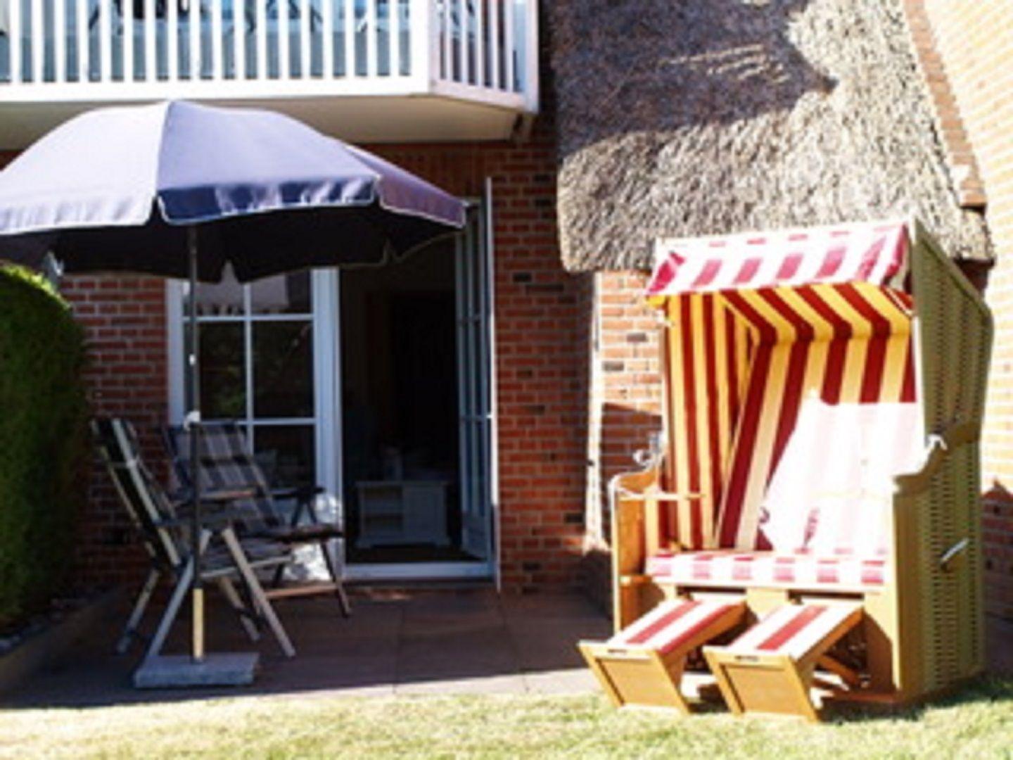 Terrasse mit Sonnenschirm, Stühlen und Strandkorb vor einem Haus mit Dach aus Stroh.