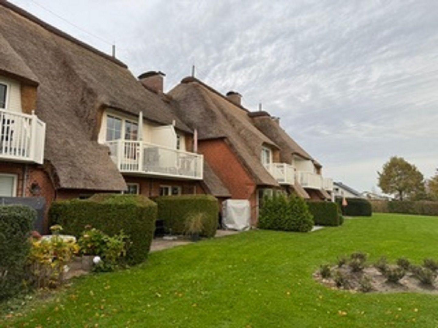 Reihenhaus mit Strohdach und weißen Balkonen vor grünem Rasen.