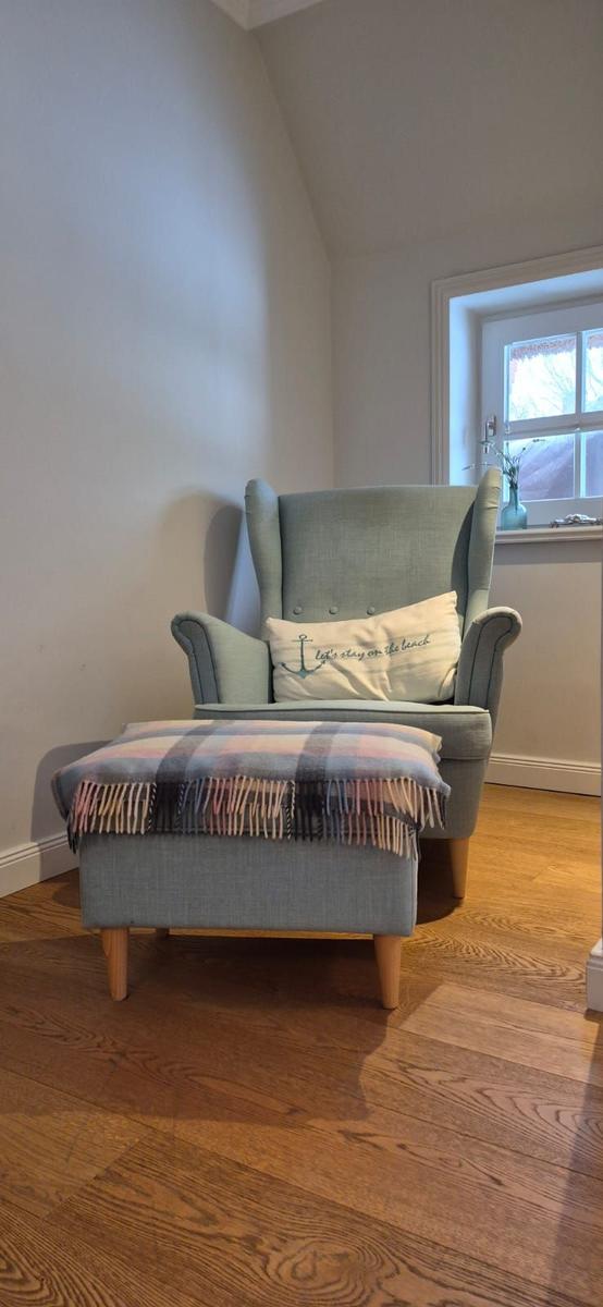 Ein grauer Sessel mit Kissen und Fußhocker auf Holzboden.