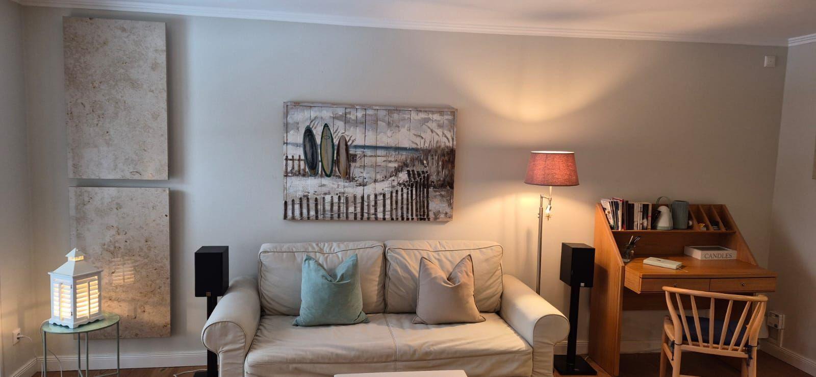 Wohnzimmer mit Sofa, Schreibtisch und Wandbild mit Surfbrettern.
