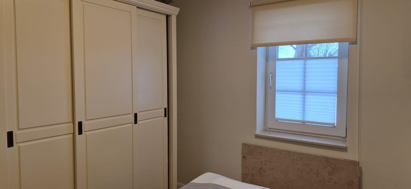 Schlafzimmer mit Kleiderschrank und Fenster mit Rollladen.