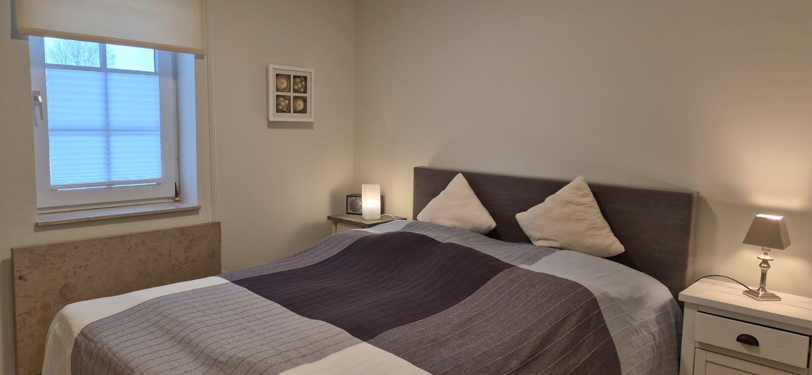 Schlafzimmer mit Bett, Nachttisch und Fenster mit Jalousie.