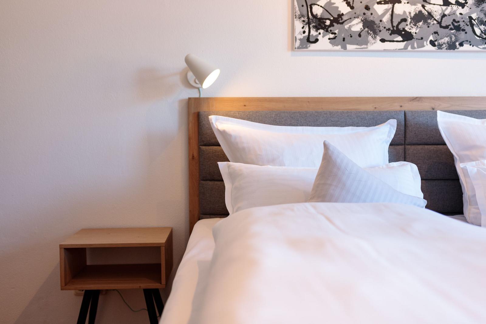 Schlafzimmer mit Bett, Nachttisch und Wandlampe. Wandbild über dem Kopfteil.