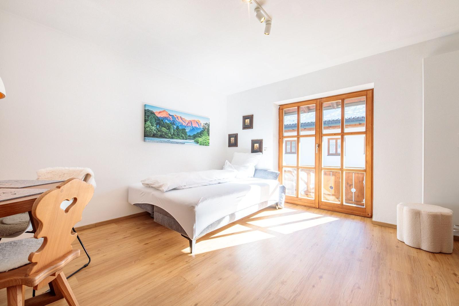 Schlafzimmer mit Bett, Holzboden und Glas-Tür zur Terrasse.